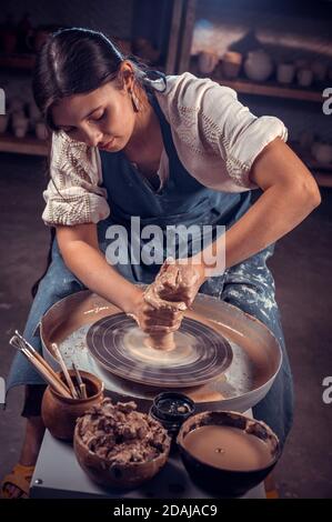 Elegante scultore vasaio professionale lavora con argilla sulla ruota di un vasaio e a tavola con gli attrezzi. Lavoro manuale. Foto Stock