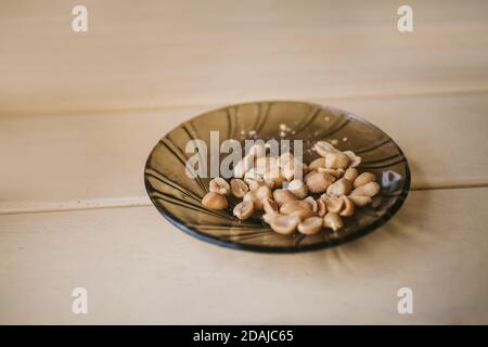 Arachidi salate in un piatto di vetro su un tavolo bianco. Spuntini veloci salati. Foto Stock