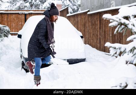 donna con pala che pulisce la neve intorno all'auto. Pala invernale. Rimuovere la neve dopo la bizzarda Foto Stock