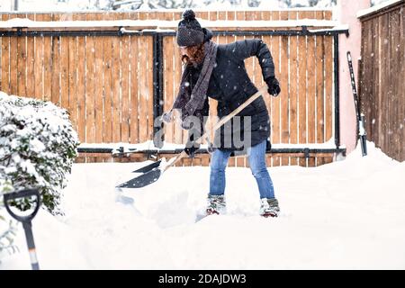 donna con pala che pulisce la neve intorno all'auto. Pala invernale. Rimuovere la neve dopo la bizzarda Foto Stock