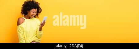 donna afro-americana sconvolto guardando smartphone sul giallo, banner Foto Stock