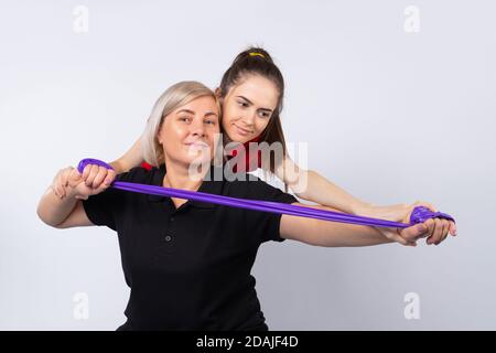 Una giovane ragazza istruttore di fitness aiuta una donna anziana a fare l'esercizio giusto. Foto su sfondo bianco. Foto Stock