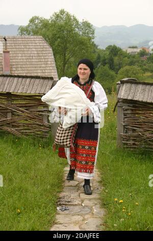 Contea di Brasov, Romania. Giovane ragazza che indossa abiti tradizionali fatti a mano cuciti a mano, portando un cuscino. Foto Stock