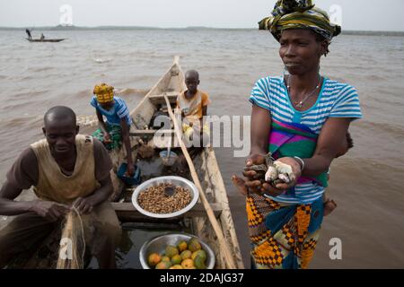 Selingue, Mali, 27 aprile 2015; pescatore Mama Kanta, 32 Con il fratello Soumara 9, e la sorella Fatouma, 14 anni. Stanno commerciando il pesce per un sacchetto delle arachidi con Djenebou Sidibe, che sta commerciando per alimentare la sua famiglia. Foto Stock