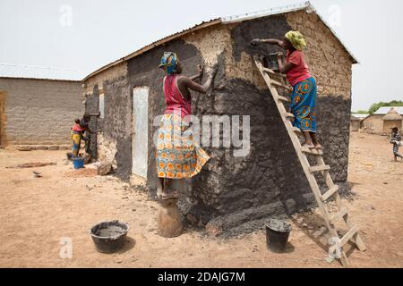 Delaba Koro, villaggio 60 km da Selingue, Mali, 27 aprile 2015; questo villaggio ha preso molte persone sfollate dalla diga. Le donne sigillano le pareti della loro casa contro le piogge imminenti con un mix liquido di fango e sterco animale. Rokia Camara, 18 anni, è in cima alla scala. Foto Stock