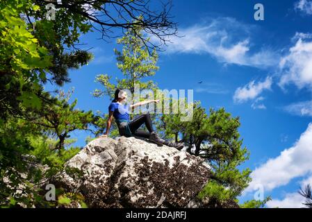 Una donna cinese seduta su uno sperone roccioso coperto di lichen in cima alla montagna monumento nel grande barrington massachusetts in una giornata di sole. Foto Stock