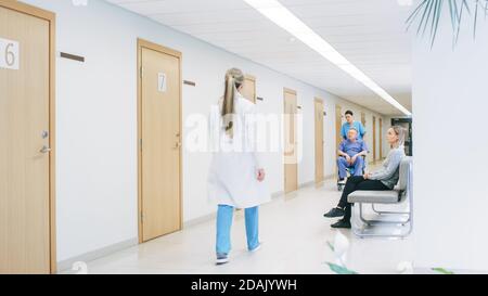 Nel corridoio dell'ospedale, il personale professionista occupato che cammina vicino, l'infermiere spinge l'uomo anziano nella sedia a rotelle, i pazienti aspettano il loro medico. Pulito, nuovo Foto Stock