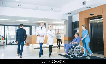 Primo piano dell'ospedale occupato, medici, infermieri e personale occupato lavoro, assistente sposta l'uomo anziano in sedia a rotelle. New Modern Medical Foto Stock