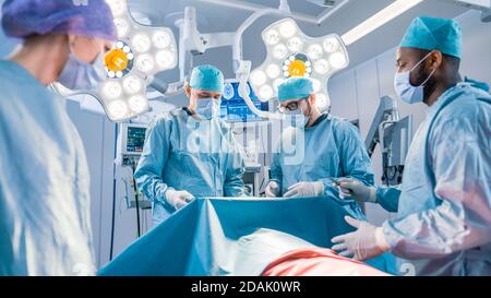 Un team diversificato di chirurgo, assistenti e infermieri professionisti che eseguono interventi di chirurgia invasiva su un paziente nella sala operatoria dell'ospedale. I chirurghi lo hanno Foto Stock