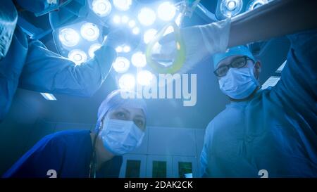 Scatto ad angolo basso di due chirurghi professionali accensione delle luci di chirurgia mentre si piega il paziente. POV Patient Shot in Modern Hospital Operating Room. Foto Stock