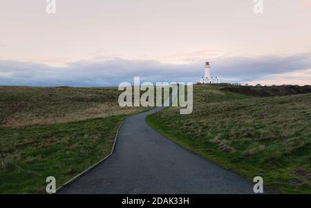 Faro sotto il cielo blu con erba e sentiero che corre in mezzo in primo piano all'alba in autunno a Flamborough, Yorkshire, Regno Unito. Foto Stock