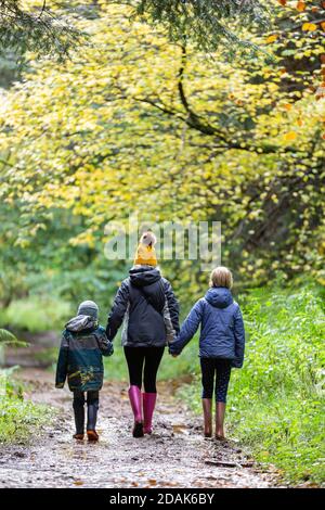 Una foto di una famiglia di tre persone che si trova a pochi passi da un bosco autunnale. Foto Stock