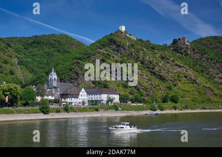 Una città lungo il fiume Reno con un castello in cima alla collina oltre e un piccolo motoscafo in primo piano, contro un cielo blu. Il fiume Reno, Germania Foto Stock