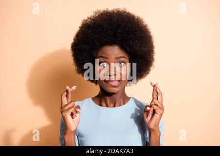 Ritratto fotografico di una donna afro-americana ansiosa che tiene le dita incrociate labbra in su isolate su sfondo color beige pastello Foto Stock