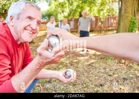 Sorridente senior giocando boules o bocce come squadra con amici in giardino Foto Stock