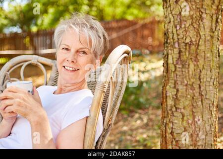 Pensò sorridente anziana con una tazza di caffè il giardino d'estate Foto Stock