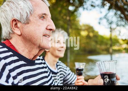 Felice coppia anziana bevendo vino in natura presso il lago il fine settimana Foto Stock