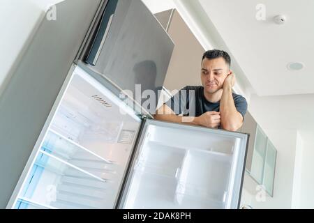 Il ragazzo è triste vicino al frigorifero vuoto senza cibo. Pubblicità del servizio di consegna del cibo. Foto Stock