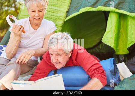 Libro di lettura della coppia anziana insieme davanti alla tenda sopra Campeggio vacanza all'aperto Foto Stock