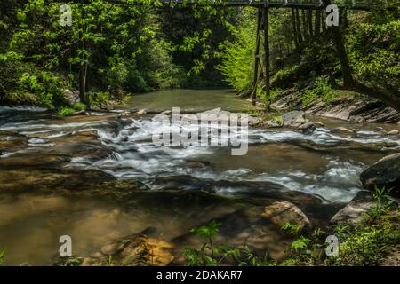 Due uomini che pescano sotto il ponte di sentiero sullo sfondo lontano dalle rapide acque tumbling del fiume in una giornata luminosa e soleggiata in primavera Foto Stock