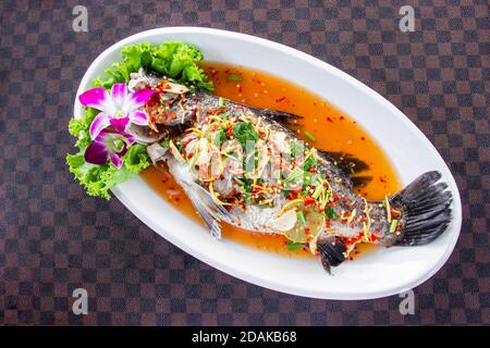 Pesce di spigola al vapore con limone mettere un piatto bianco di ceramica sul pavimento di pelle il motivo griglia. Vista dall'alto. Foto Stock