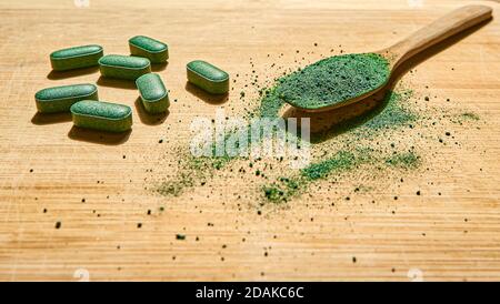 Polvere di clorella in un cucchiaio di legno e pillole di spirulina su uno sfondo di legno chiaro. Supplemento nutrizionale, Detox superfood Foto Stock