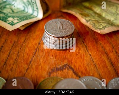 Pila di monete - sulla parte superiore è un dollaro di quarto degli Stati Uniti. In primo piano è una pila di monete non specificate e una nota di carta nella carta di sfondo Foto Stock