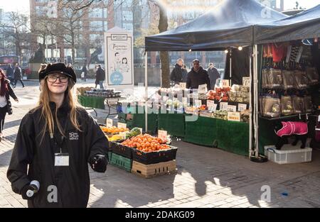 Un mugger di beneficenza fortemente illuminato sul retro si trova di fronte ad una bancarella di frutta e verdura, picadilly Gardens, manchester Foto Stock