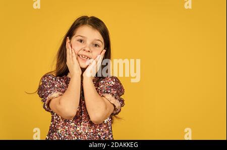 Faccia preziosa. Bambino tira le guance in su nell'affetto. Ragazza sorriso carino su sfondo giallo. Concetto di infanzia e felicità. Capretto con spazio allegro copia faccia. Felice giorno per i bambini. Infanzia felice. Foto Stock