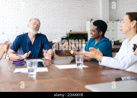 Felice squadra di multi-etnico dedicato di medici professionisti applaudendo il loro medico capo. Foto Stock