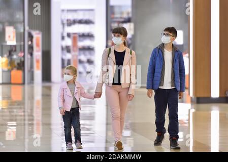 Mamma e bambini camminano attraverso il centro commerciale indossando maschere Foto Stock
