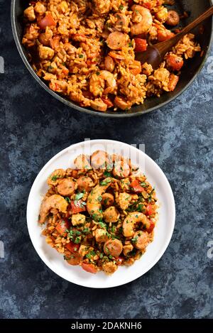 Creola jambalaya con riso, salsicce affumicate, carne di pollo e verdure su sfondo di pietra blu. Vista dall'alto, disposizione piatta, primo piano Foto Stock