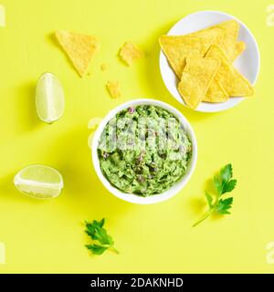 Guacamole immergere in ciotola su sfondo giallo. Diffusione sana dell'avocado. Vista dall'alto, disposizione piatta Foto Stock