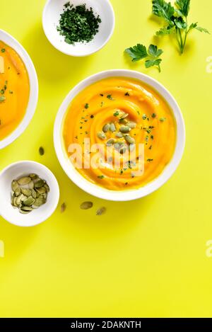 Purea di zucca con semi in ciotola su sfondo giallo con spazio di testo libero. Concetto di alimentazione sana. Vista dall'alto, disposizione piatta Foto Stock