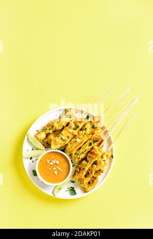 Spiedini di pollo alla griglia serviti con salsa di arachidi. Satay di pollo con salsa di arachidi. Pasto gustoso per cena o antipasti di festa. Backgroun giallo Foto Stock