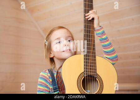 Una bambina sbirciata da dietro una custodia per chitarra a casa. Foto Stock