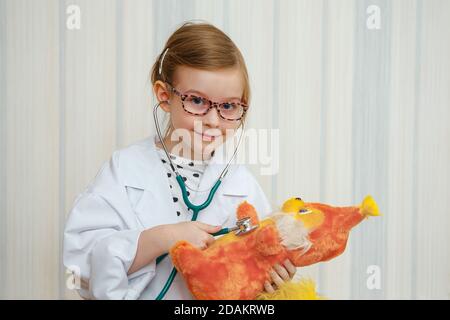 Una bambina in un cappotto del medico sorride e invita ad essere trattata. Gioco medico educativo. Foto Stock