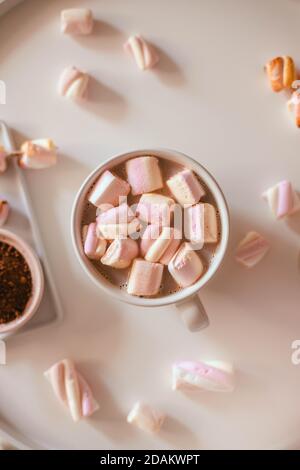 Tazza in ceramica di cioccolato caldo o cacao con marshmallow su un tavolo bianco. Decorazioni ghirlande di luci. Disposizione piatta, vista dall'alto Foto Stock