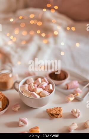 Decorazioni ghirlande di luci. Tazza in ceramica di cioccolato caldo o cacao con marshmallow su tavola bianca. Foto Stock