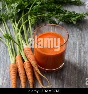 Succo di carote appena spremuto da una carota giovane in un bicchiere su un tavolo di legno, fuoco selettivo Foto Stock
