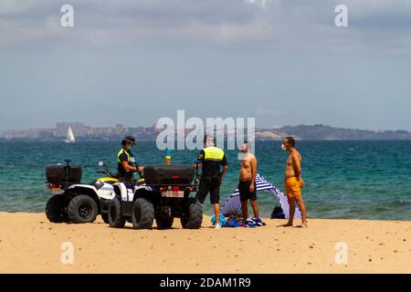 Alicante, SPAGNA - 8 agosto 2020 due agenti di polizia locali che pattugliano la spiaggia di Urbanova su un quad, detengono due persone sospettate di rubare i beni Foto Stock