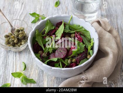 Insalata di barbabietole con cipolla rossa al forno, capperi, crescione, verdure e salsa vinaigrette. Cibo vegano sano. In una ciotola blu su un tavolo di legno Foto Stock