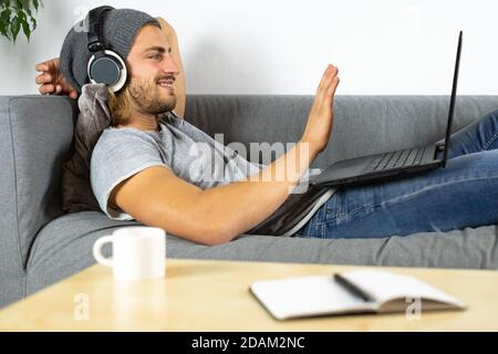 Bel giovane uomo caucasico che lavora a casa usando un computer portatile e parlare con il telefono cellulare dicendo ciao Foto Stock