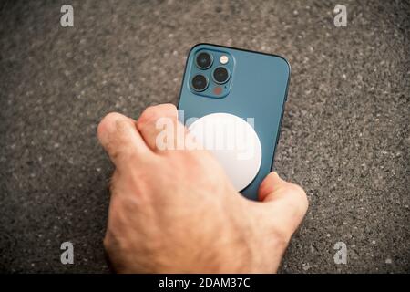 Parigi, Francia - Novembre 11, 2020: Uomo che posiziona dispositivo di ricarica MagSafe Wireless Charger l'ultimo modello di smartphone iPhone 12 Pro Max 5G di Apple computer primo piano di Pacific Blue Mobile Phone Device - sfondo in ceramica Foto Stock