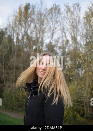 Bella giovane donna che lancia i suoi capelli lunghi biondi in autunno Parcheggio Foto Stock