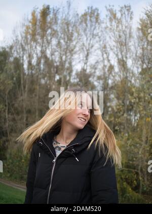 Bella giovane donna che lancia i suoi capelli lunghi biondi in autunno Parcheggio Foto Stock