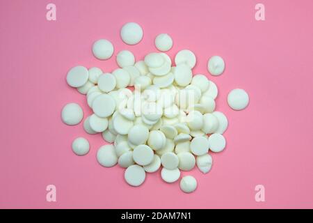 Gocce di cioccolato bianco su sfondo rosa. Gocce bianche di cioccolato per la preparazione della glassa. Cioccolato bianco per pasticcerie vista dall'alto. Foto Stock