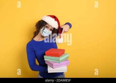 Ragazza felice con maschera facciale riceve regali di Natale. Sfondo giallo Foto Stock