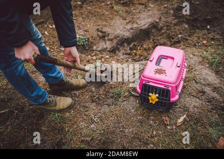 Scena Spooky al cimitero degli animali domestici. La tomba di amici animali perduti. Compagnia, addio. Un uomo porta un animale domestico morto in un vettore alla foresta e. Foto Stock