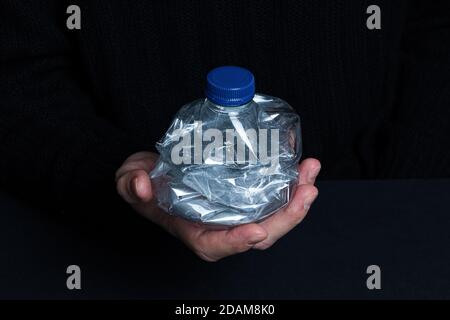 La mano che tiene la bottiglia vuota di plastica schiacciata isolato su un nero sfondo Foto Stock